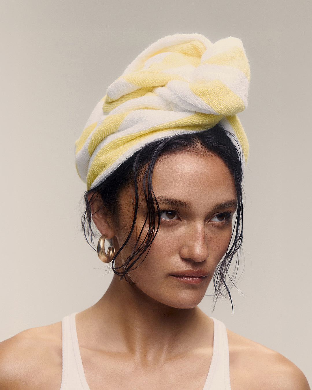 Woman with a yellow and white towel wrapped around her head against a neutral background